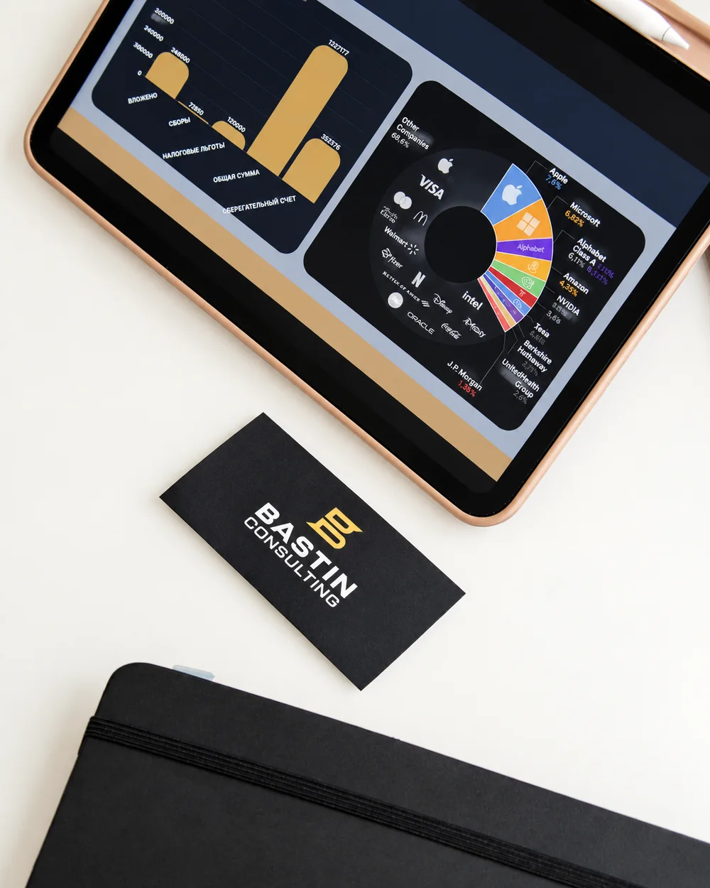 A Bastin Consulting card on the desk beside a tablet showing spending and portfolio charts.